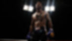 Boxer with tattoos stands in a dimly lit ring, wearing blue gloves and shorts. Bright overhead lights create a dramatic atmosphere.