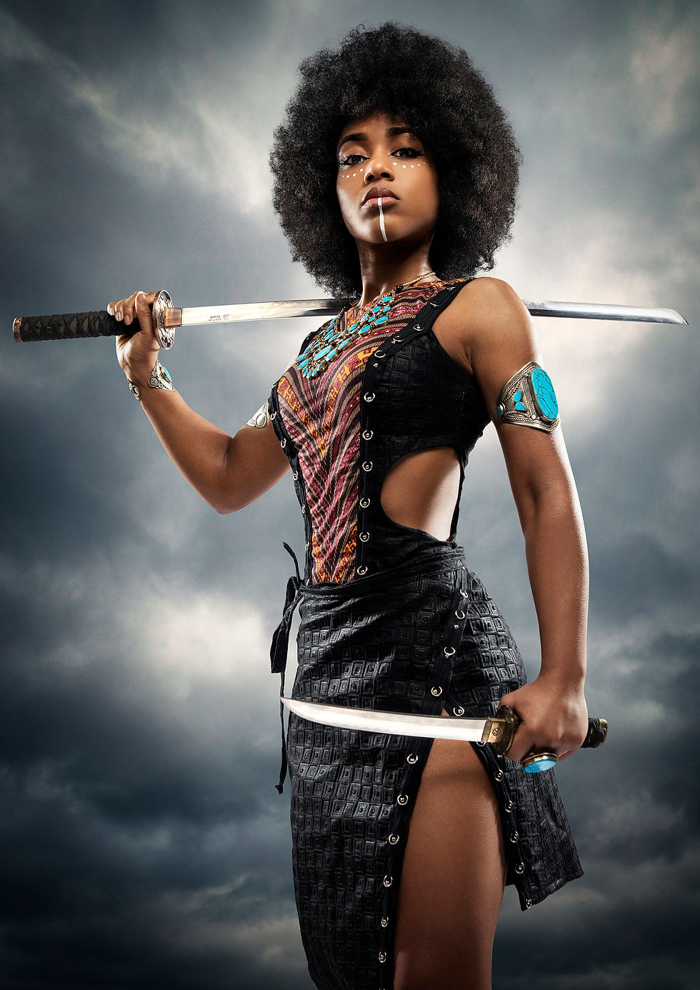 Warrior woman with an afro holds two swords, wearing a patterned dress and turquoise jewelry. Cloudy sky background, fierce expression.