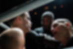 Boxer sits in a corner with a serious expression as two coaches give intense guidance. Dimly lit boxing ring, focus on their intense faces.