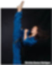 A person in a blue martial arts uniform performs a high kick against a dark backdrop, exhibiting intensity and skill.