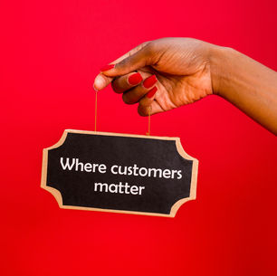 Hand with red nails holding a black sign reading "Where customers matter" against a vibrant red background.