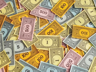 Colorful Monopoly money in various denominations scattered randomly. Bills show values like 500, 100, 50. Multicolored, playful scene.