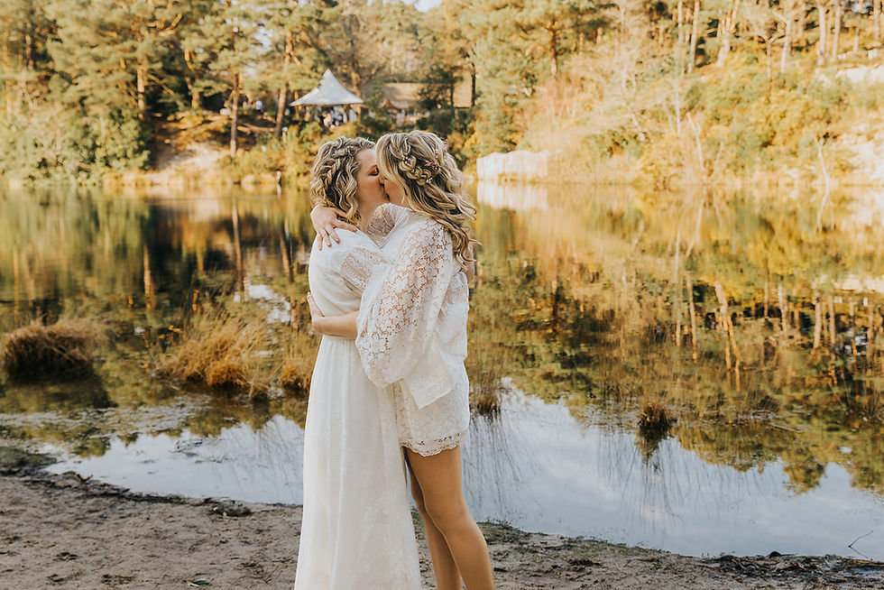 an all female couple kissing by a lake, both wearing white wedding dresses