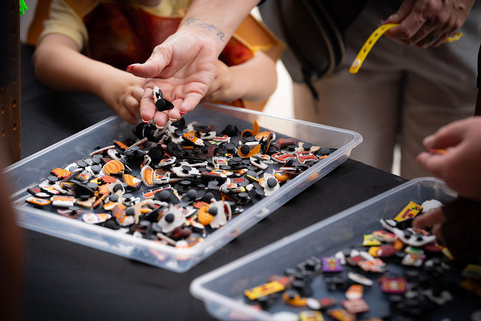 Hands sort through colorful Jibbitz trays on a black table. A child reaches in.