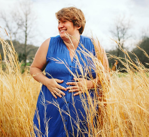 Pregnant preson in blue dress standing in field of grains. 