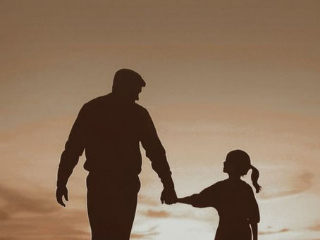 Pai e filha de mãos dadas ao pôr do sol, representando o vínculo afetivo, a presença paterna e a construção da segurança emocional da filha.