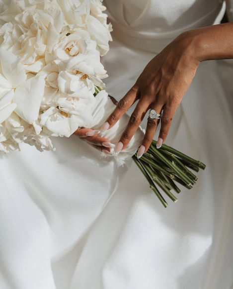 Bride's hands holding white wedding bouquet, diamond ring