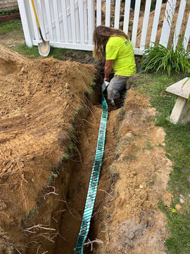 Worker laying utility tape in a dirt trench.