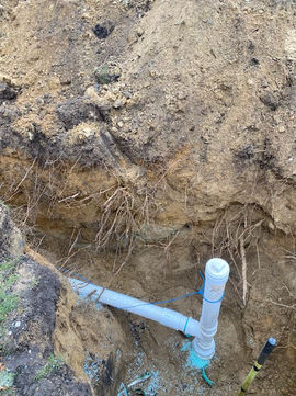 White PVC drainage pipe installed in an earthen trench.
