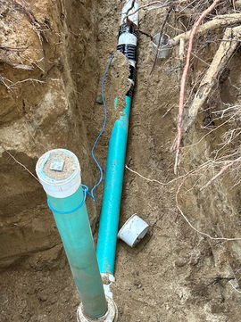 Installed turquoise PVC sewer pipes in an open dirt trench.
