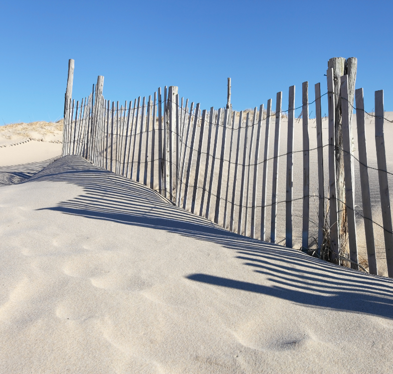 A light sandy beach on a bright, clear day with a wooden fence.
