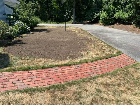Curved red brick path next to a freshly leveled lawn.