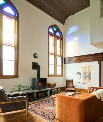 Living room in converted church with restored stained glass windows & wood-burning stove