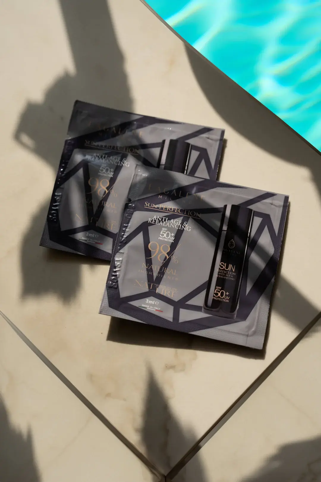 Due confezioni di Mini Sun Perfection su superficie chiara vicino a una piscina con riflessi di luce.