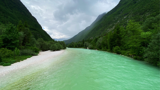 Fluss Soča in Slowenien, umgeben von grünen Bergen und Wäldern. Die türkisfarbene Farbe des Wassers spiegelt die natürliche Schönheit der Region wider.