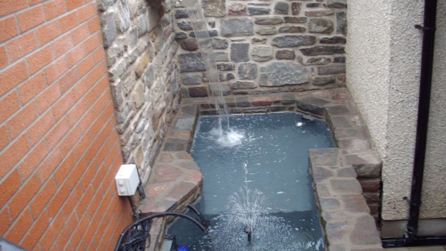 Finished Almondsbury pond with centre water feature waterfall from stonework wall completed by Ivanhomes builders garden view