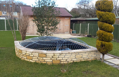 Stone wall enclosed pool with netting in a garden, house extension.