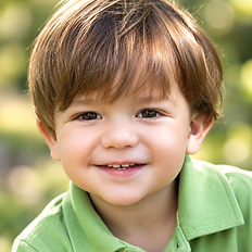 Outdoor headshot of a smiling young boy with brown hair wearing a green polo shirt.