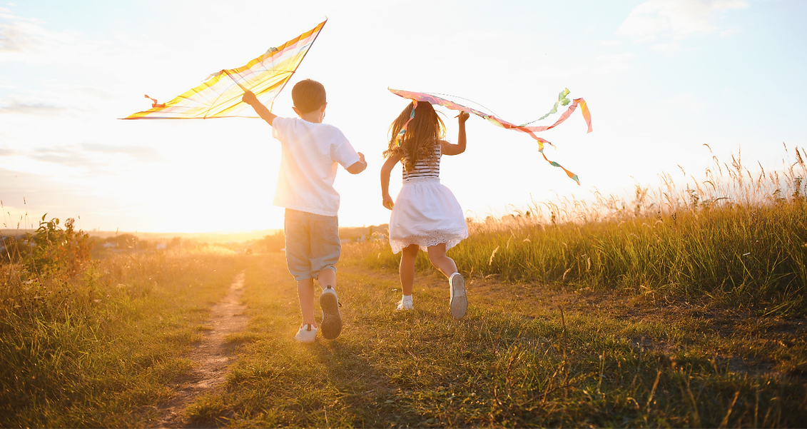 Zwei Kinder laufen mit Drachen über eine Wiese – freie Bewegung und Wohlfühlen in passender Kleidung, genäht mit Federkinder-Schnittmustern.