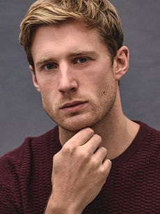 Freddie - headshot of male model with textured blonde hair, stubble, and wearing a zip-up black hoodie, represented by ROC Talent Agency UK