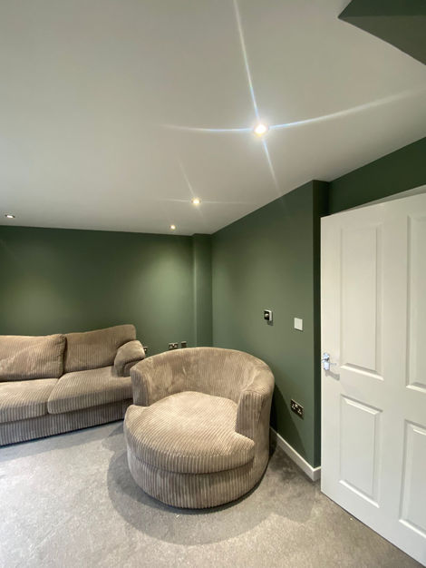 A modern living room with deep green painted walls, a white ceiling with recessed lighting, and a wooden coffee table against a freshly decorated backdrop. The high-quality paint job and expert finishing create a sophisticated and inviting space.