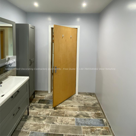 Modern bathroom featuring wood-look tiles, sleek white paint, a chrome towel radiator, and a clean shower space. The design showcases JDC Ltd’s expert bathroom decorating services in Bradford, with a focus on contemporary style and high-quality finishes