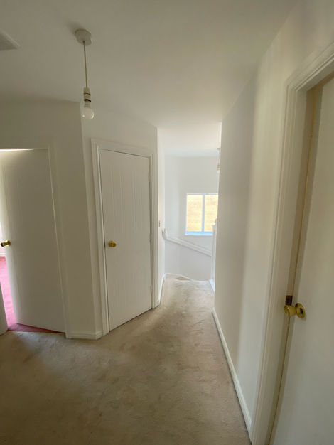 Freshly painted upper hallway showcasing clean white walls, modern minimal light fixtures, and deep contrast carpet. A tidy, welcoming space connecting the upstairs rooms.