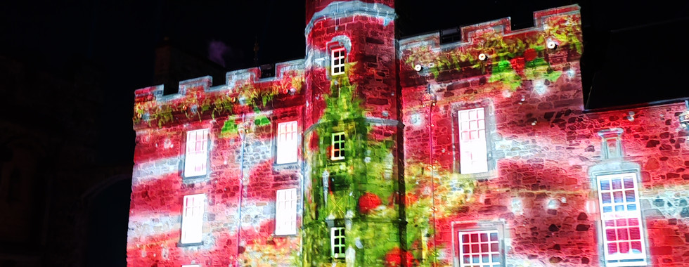 Castle façade lit with vibrant red and green light projection at night, featuring white window frames and a clock tower.