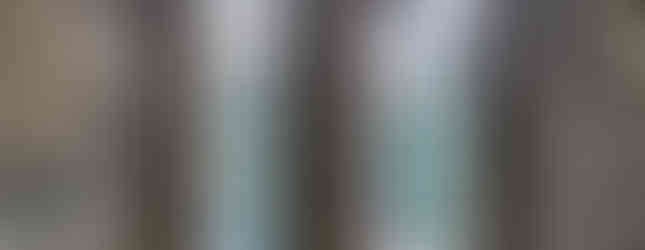 Rustic stone room with two tall, arched windows revealing a view of trees and rooftops. The setting is medieval, with an aged, historic feel.