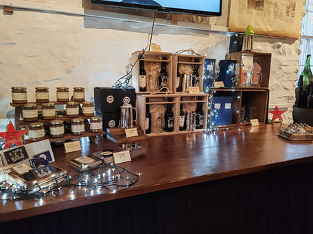 Jars, mugs, and gift boxes on a wooden counter with fairy lights. Red stars indicate a 10% discount. Rustic white wall background.