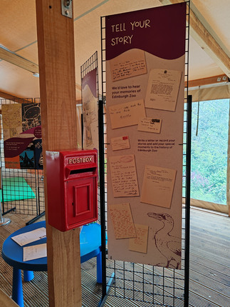 Red postbox beside Tell Your Story display of handwritten letters and postcards at Edinburgh Zoo, in a bright exhibit tent.