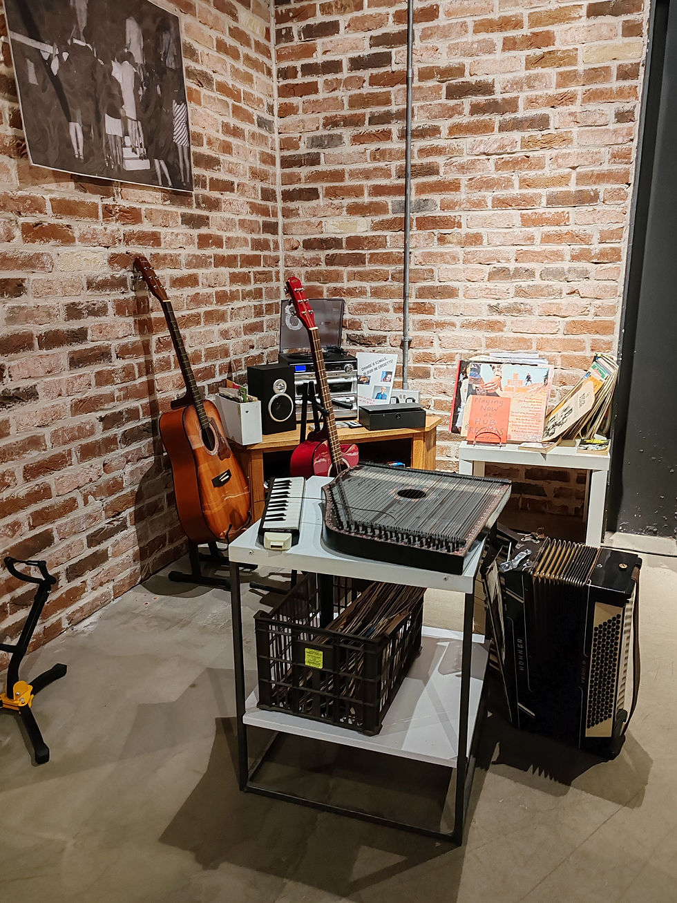 Musical corner with guitars, melodica, zither, records, and accordion on tables against brick walls. Vintage vibes with retro gear.