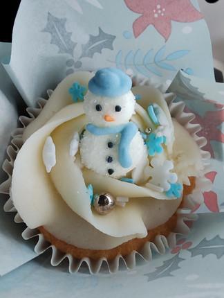 Cupcake with white frosting and a small snowman decoration, adorned with blue and white snowflake sprinkles and a silver ball.