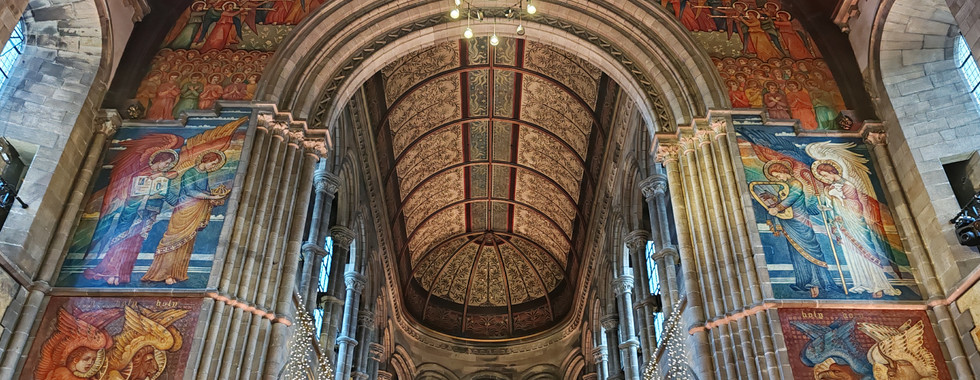 Ornate church interior with colourful murals of angels and religious scenes on stone walls. Decorative lights hang from the arched ceiling.