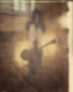 A skeleton with a hat and wig plays guitar in a dimly lit stone-walled room, creating an eerie and vintage mood.