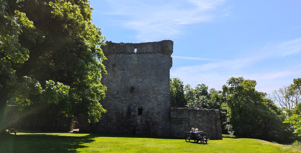 A view of the grounds of Lochleven Castle in the foreground and the Tower House in the background.