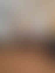 Vintage room with a grand piano, sheet music, and a soft-lit lamp. A painting and decorative sword are above a lit fireplace, creating a cosy atmosphere.