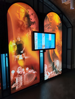 Illuminated orange panels with images of people playing musical instruments and various sports, and a TV screen displaying text.