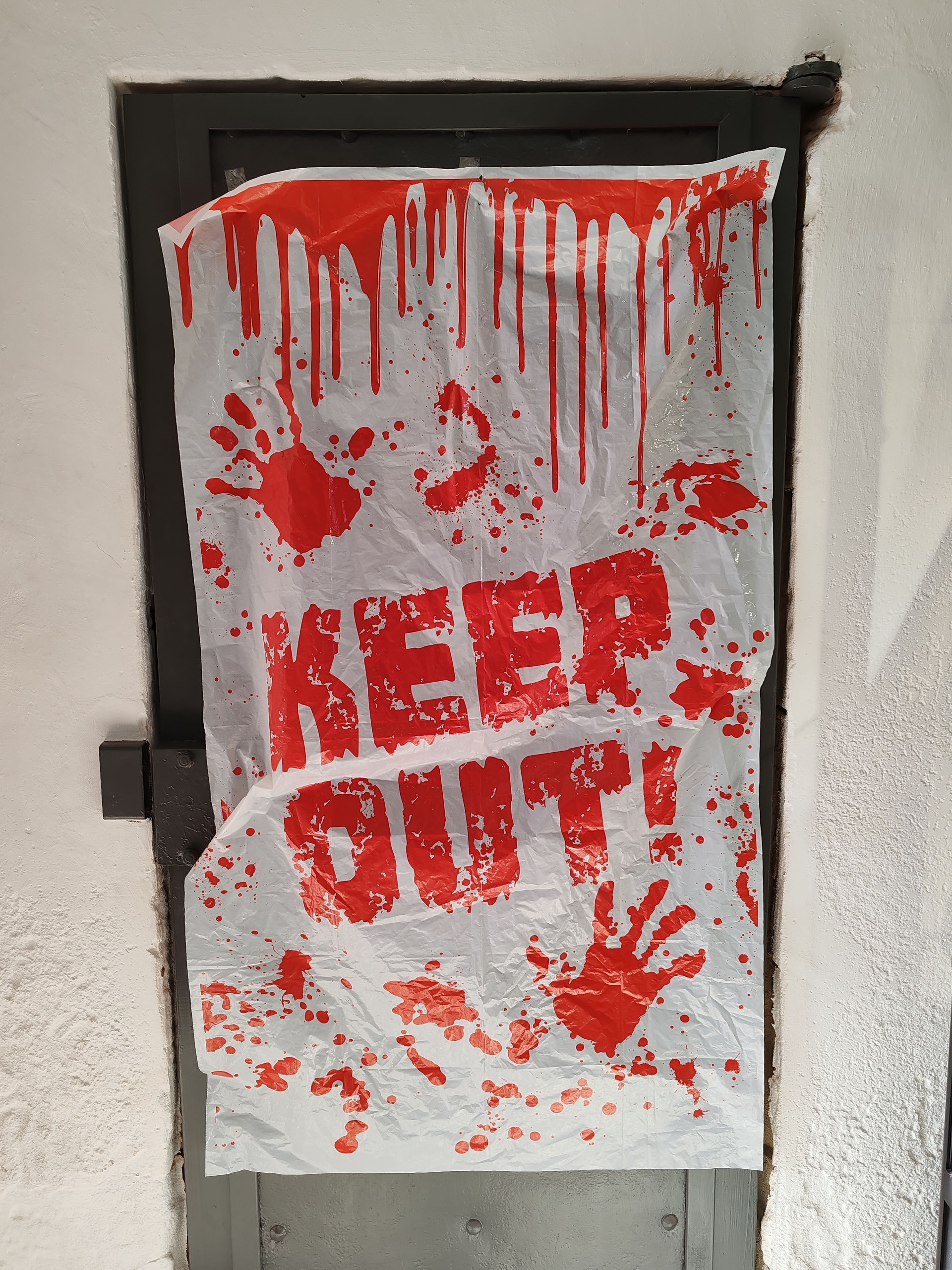 White door covered with a tattered sign that reads "KEEP OUT!" in red, with red handprints and splatter, creating a creepy vibe.