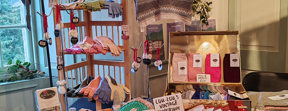 Knitted items displayed in a cosy shop setting, featuring colourful hats and gloves. A sign reads "Lou-Lou's Vintage Emporium."