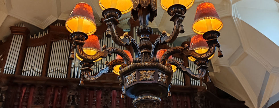 Ornate chandelier with orange lampshades hangs from an intricate ceiling in an opulent room, featuring stained glass windows and carved wood details.