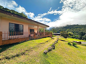 Single-story home with covered porch and green lawn, overlooking cloud-draped forested mountains in the Chirripó Valley, Costa Rica.