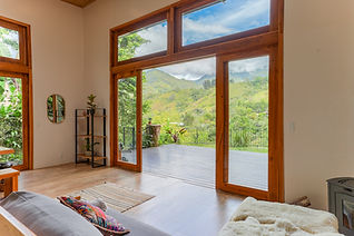 Bright living room with floor-to-ceiling wood-framed glass doors opening to a deck with sweeping Chirripó mountain views in Costa Rica.
