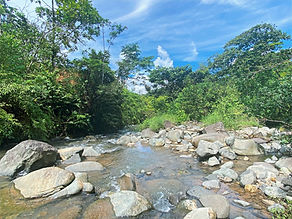 Shallow rocky river with boulders and clear water winding through tropical forest on a riverfront property in Pérez Zeledón, Costa Rica.