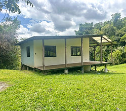 Elevated starter home with covered wood deck and corrugated roof, set on a green pasture bordered by forest in Pérez Zeledón, Costa Rica.
