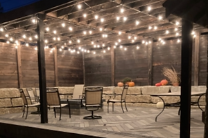 Evening view of a hardscape patio with pergola lighting, stone seating wall, and paver sur