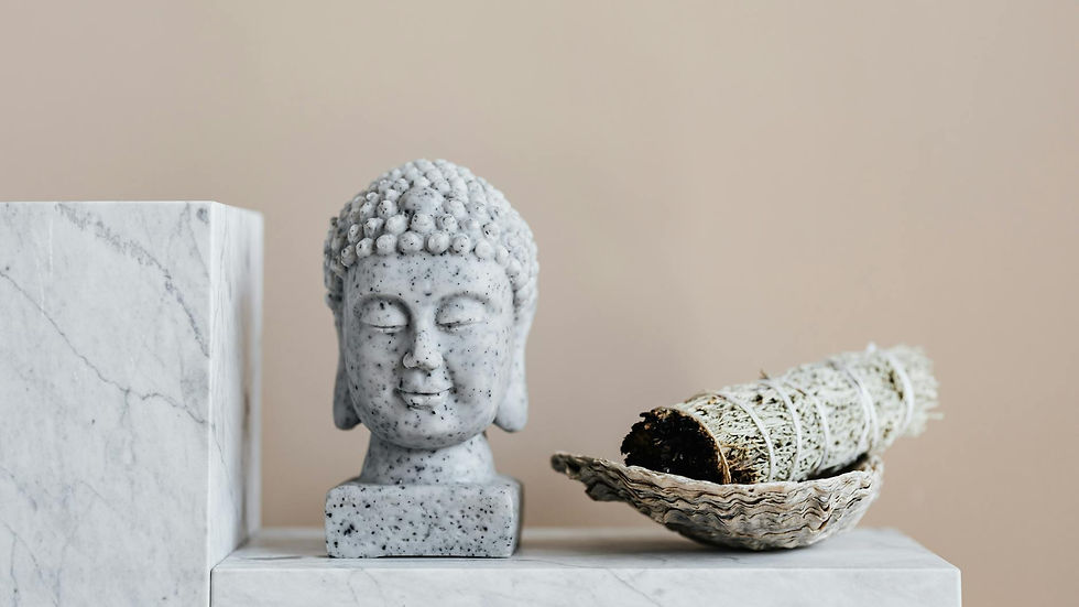 Granite bust of Buddha placed on white marble shelf near sage bundle in bowl against against beige wall as religion objects and house decoration elements