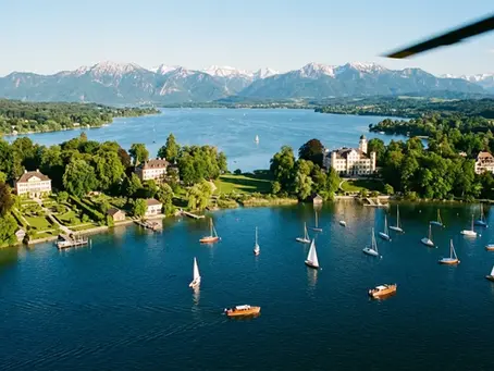 Elegante Luftaufnahme des Starnberger Sees aus Hubschrauberperspektive, klarer Sommertag, tiefblaues Wasser, grüne Ufer, Alpenpanorama im Hintergrund, natürliches Licht, hochwertige Fotografie, luxuriöse Stimmung