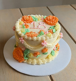 Custom smash cake with white swags paired with orange buttercream roses. Green, pink, and yellow buttercream decor. “18” wrote on the top