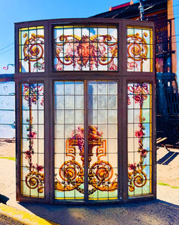 Ventana antigua de hierro forjado con vitral artístico, representando un sátiro mitológico en estilo clásico europeo.